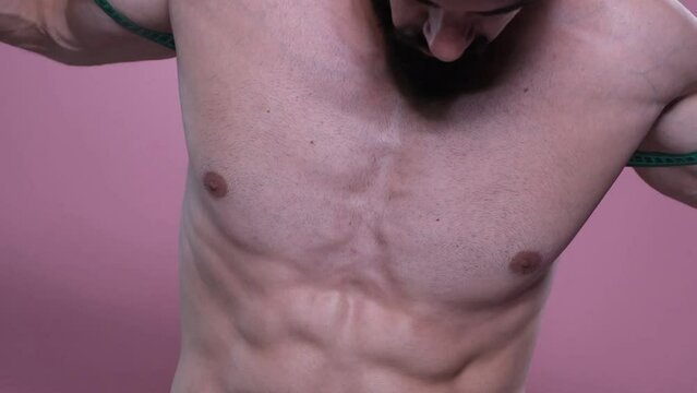Strong shirtless bodybuilder measuring his chest width with a measuring tape, comparing the results and gains, , pink background