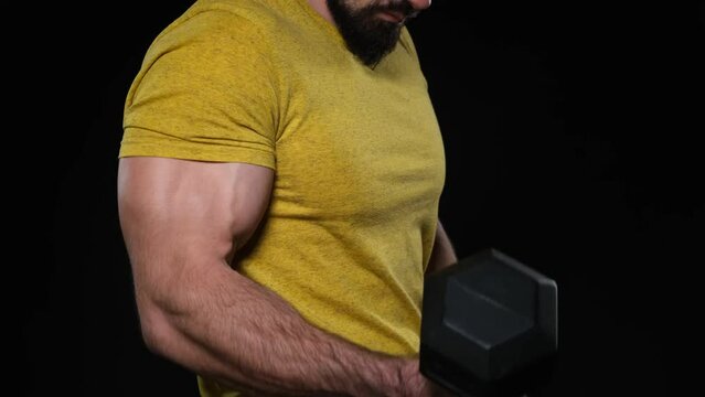 Young bodybuilder in a yellow T-shirt lifting a heavy dumbbell, studio image, dark background, dramatic atmosphere
