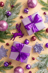 Christmas concept. Top view vertical photo of lilac gift boxes pink violet baubles flower snowflake deer ornaments sequins and pine branches in snow on isolated pastel beige background
