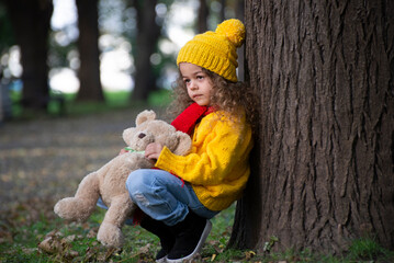 Sad little girl with a teddy bear in the park