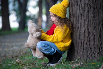 Portrait of a little girl with a bear playing in an autumn park