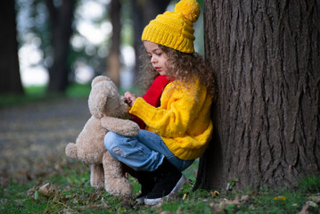 Sad little girl with a teddy bear in the park