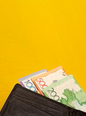 Vertical banner with paper money of the Republic of Kazakhstan. 2000, 5000, 10000 tenge in black leather men's wallet on yellow textile background. Concept of relocation, immigration, tourism. Cash