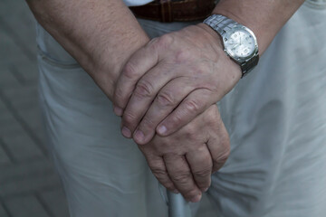 The large hands of an elderly man are folded on a cane with a watch on his right hand..