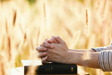 A Christian praying with his hands together on the holy bible on Thanksgiving Day and the sunset...