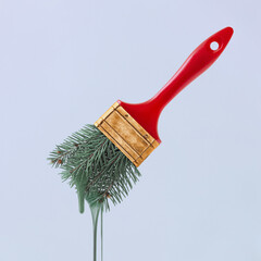 Dark green paint leaking from Christmas tree leaves forming bristles of brush with a gold red colored handle. Creative abstract Xmas greeting card. Minimal aesthetic concept. Pastel purple background.
