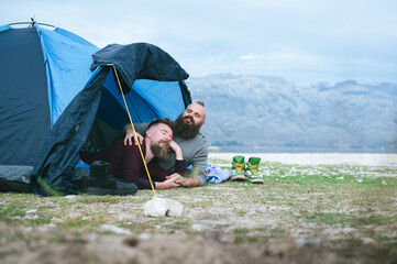 Attractive male gay couple camping by the sea under amazing mountain view. Hipsters homosexuals...