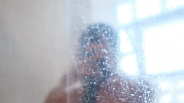 Rear view of a naked woman washing her hair with shampoo while taking a shower