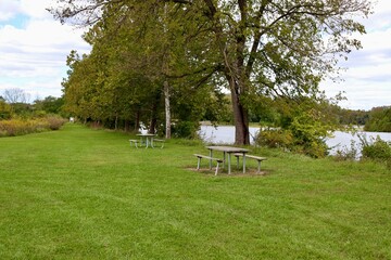 The empty tables near the river in the park.