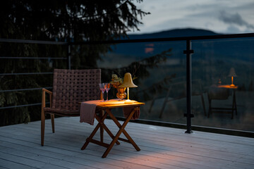 Spacious terrace with cozy table, chair and lamp highly in mountains at dusk. Cozy lounge place for rest at house on nature
