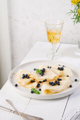 Pancakes with blueberries and mint on a plate. White wooden table. Light background. Serving a rustic table with yellow flowers and a yellow drink