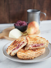 grilled sandwich with red onions, pears and cheese; served in half with ingredients in the background on a wooden cutting board
