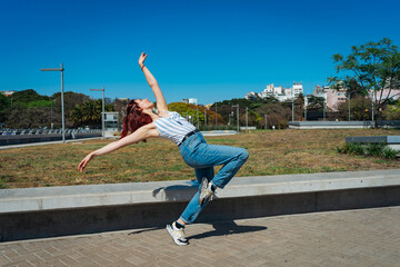 Fototapeta na wymiar Beautiful young latina dancing happily in the street while partying with jumps and somersaults. Concept of joy, street dance, hip hop.