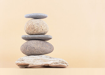 Fototapeta na wymiar Stack of rocks on a beige background. Balancing pyramid of five sea stones, front view, copy space. Harmony, balance, spa therapy, zen concept.