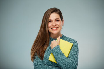 Smiling woman student in warm sweater holding yellow book. Advertising female studio portrait.