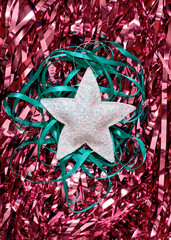 Minimalistic Christmas composition. The glitter star decoration, along with a green ribbon, is on a red shiny tinsel. Abstract layout for New Year or Christmas poster, banner, postcard. Flat lay.