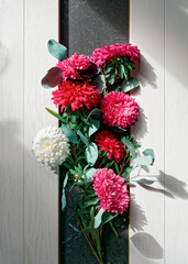 A bouquet of red, pink, white asters and dry eucalyptus branches is on a white wooden background. Autumn composition, thanksgiving day concept.