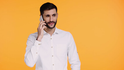 bearded man in white shirt talking on smartphone isolated on yellow