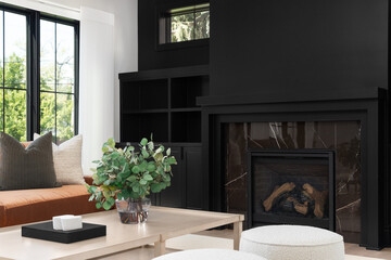 A cozy living room detail shot with a leather couch and wood table in front of a black built-in shelving and fireplace.
