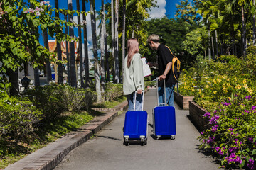 Young Asian couple tourists dragging luggages looking at map finding hotel destination, Tourist Vacation Concept