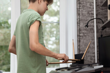 A teenage boy is a young musician, playing on the installation of electronic drums with sticks,...