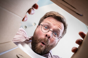 Man has unpacked a delivered package, looks at the contents with a surprised and funny expression....