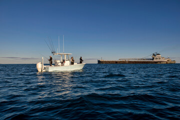 People fishing on a boat with a freighter in the background.