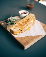 A focaccia bread salami toastie served with pickle, salad and a coffee in a cafe environment.