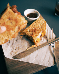 A focaccia bread salami toastie served with pickle, salad and a coffee in a cafe environment.