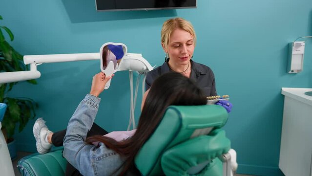 Woman Professional Dentist Examines a Smiling Female Patient in a Dental Clinic. Selects the Shade of Dental Implants Before Operation. Concept of Healthcare and Medicine. Slow Motion.