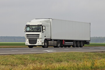 White semi truck drive on countryside highway road on green field at autumn day. Front side view ....