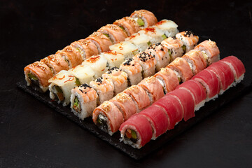 Assortment of different kinds of sushi rolls placed on black stone board. Sushi set with salmon, cucumbers, cream cheese, avocado and sesame seeds. Sushi image for menu