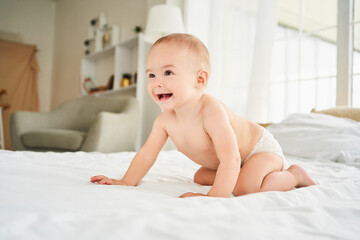 Smiling handsome toddler boy crawling on bed in bedroom.