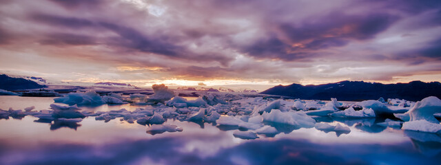 Wide panorama landscape shot of a moody winter sunset of iceberg and icy sea water with colorful clouds from Iceland  © Thorin Wolfheart