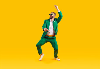 Fototapeta na wymiar Happy young guy having fun at crazy St Patrick's Day holiday party. Full body shot of funny, cheerful, goofy man wearing green suit and sunglasses dancing isolated on bright yellow colour background