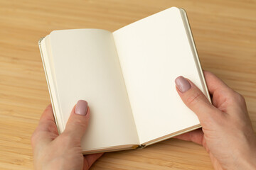 A notebook with blank pages in a woman's hands. A woman is holding an open notebook. A woman's graceful hands holding a notebook.