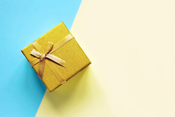 Golden gift box with bow on a blue and yellow background. Flat lay