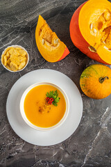 Autumn pumpkin cream soup with pumpkin spices. Delicious and bright vegetarian dish with foodstyling of fresh parsley with hot pepper and seasonings on a dark background. Menu concept, copy space