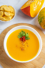 Autumn pumpkin cream soup with pumpkin spices. Delicious and bright vegetarian dish with foodstyling of fresh parsley with hot pepper and seasonings on a white background.  Menu concept, copy space