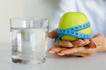 Apple with measuring tape on hand and a glass of water. Weight loss, counting calories and healthy...