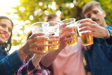 Group of four young friends cheering with beer in plastic glasses, celebrating their friendship, autumn surrounding - 539803239