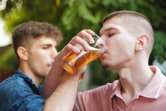 Two young friends chugging beer, drinking from a plastic cup with their arms crossed