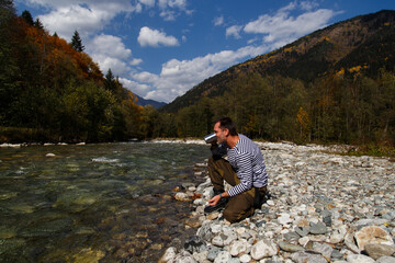 Fototapeta premium Man drinks water from a clear mountain river. He filled a metal tourist mug with water
