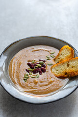 Healthy vegan pumpkin soup with red beans, pumpkin seeds, coconut cream and slices of fried bread