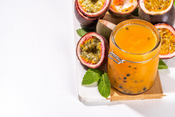 Homemade passion fruit jam in small jar, with fresh passion fruit and mint leaves on white kitchen background copy space