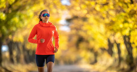 Young female athlete in sportswear runs in the park during warm indian summer