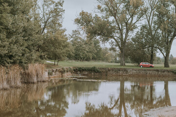 Fototapeta na wymiar Lonely Car Parked by a Natural Lake. Water Reflections 