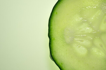 Slice of fresh cucumber close up on green background. Macro photography concept. 