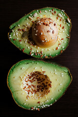 Close-up photo of a cut avocado on a dark background sprinkled with grains.