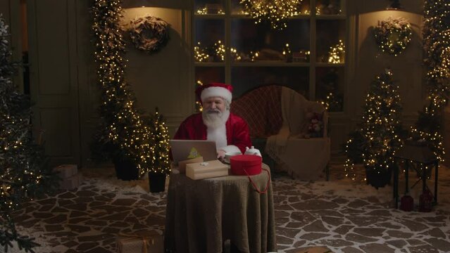 Busy Santa Claus is working in his backyard late at night, using laptop to check emails, getting ready to winter holiday season, Slow motion.